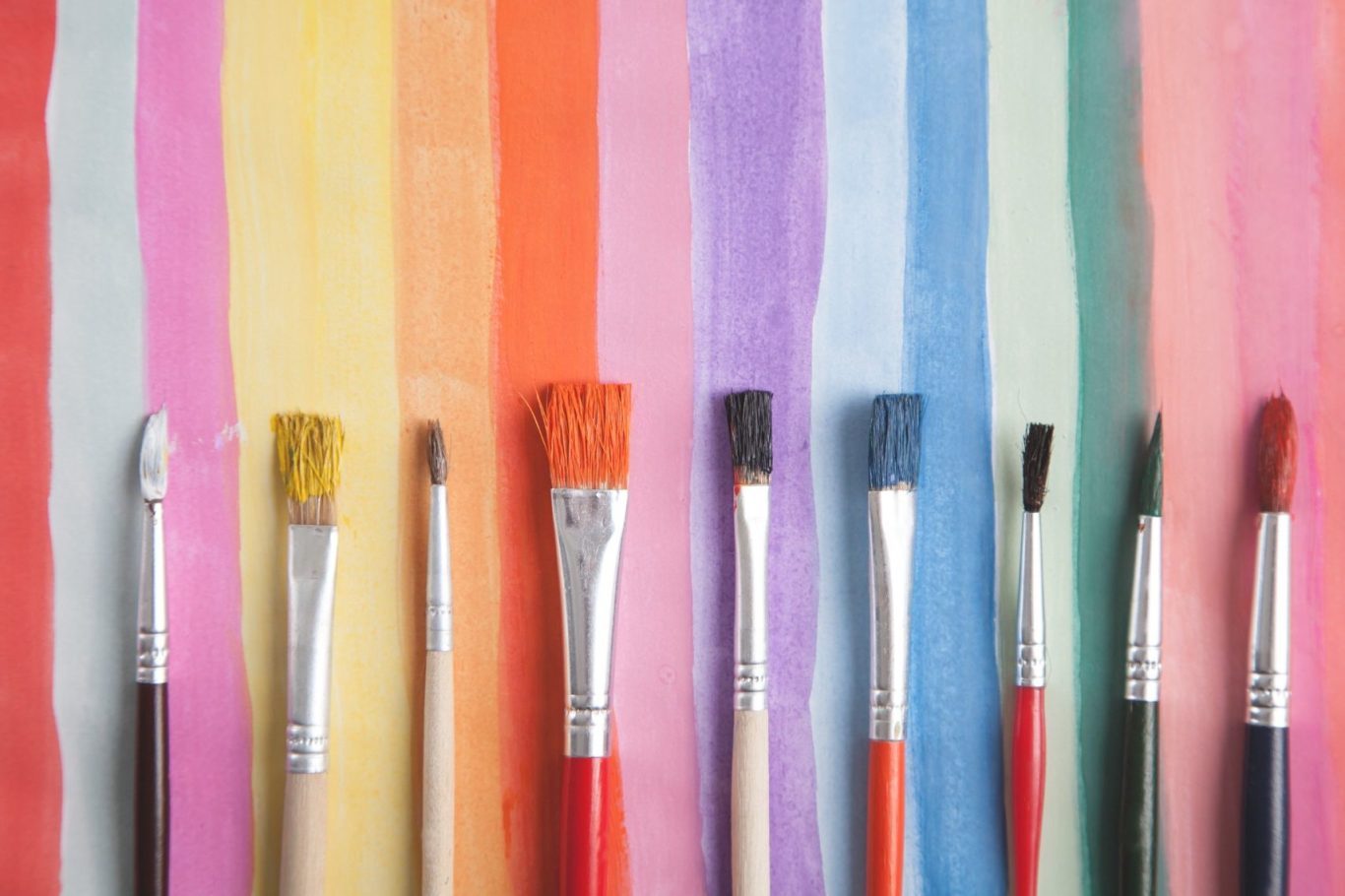 Bunte Pinsel auf gestreiftem Hintergrund in verschiedenen Farben angeordnet.